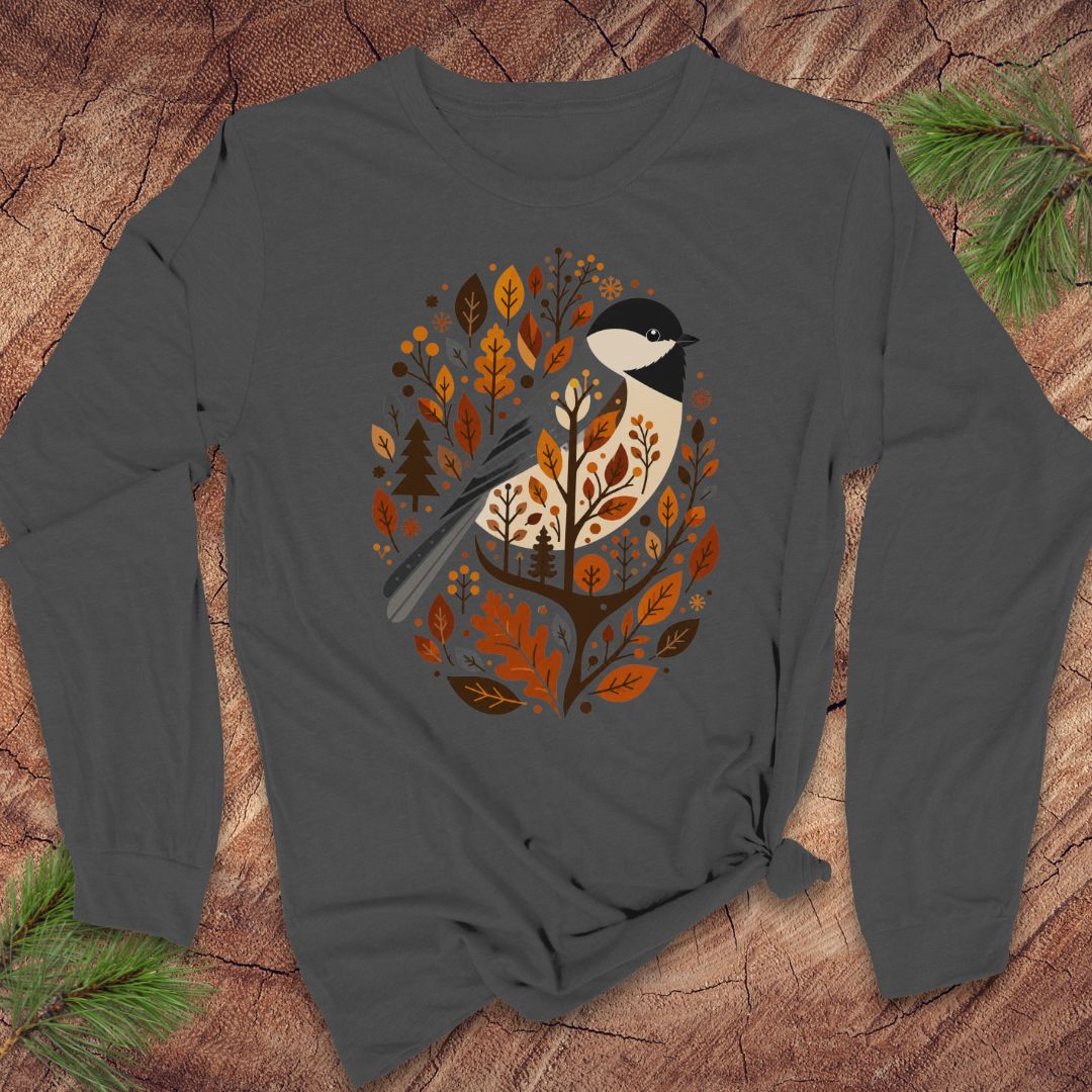 A dark gray long-sleeve t-shirt with a graphic of a bird surrounded by autumn leaves, laid flat on a rustic wood background with pine branches.