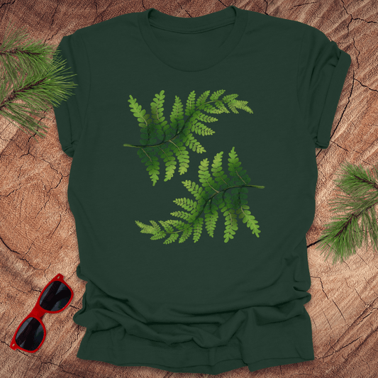 Green t-shirt with leaf design on a wooden surface with sunglasses and pine branches.