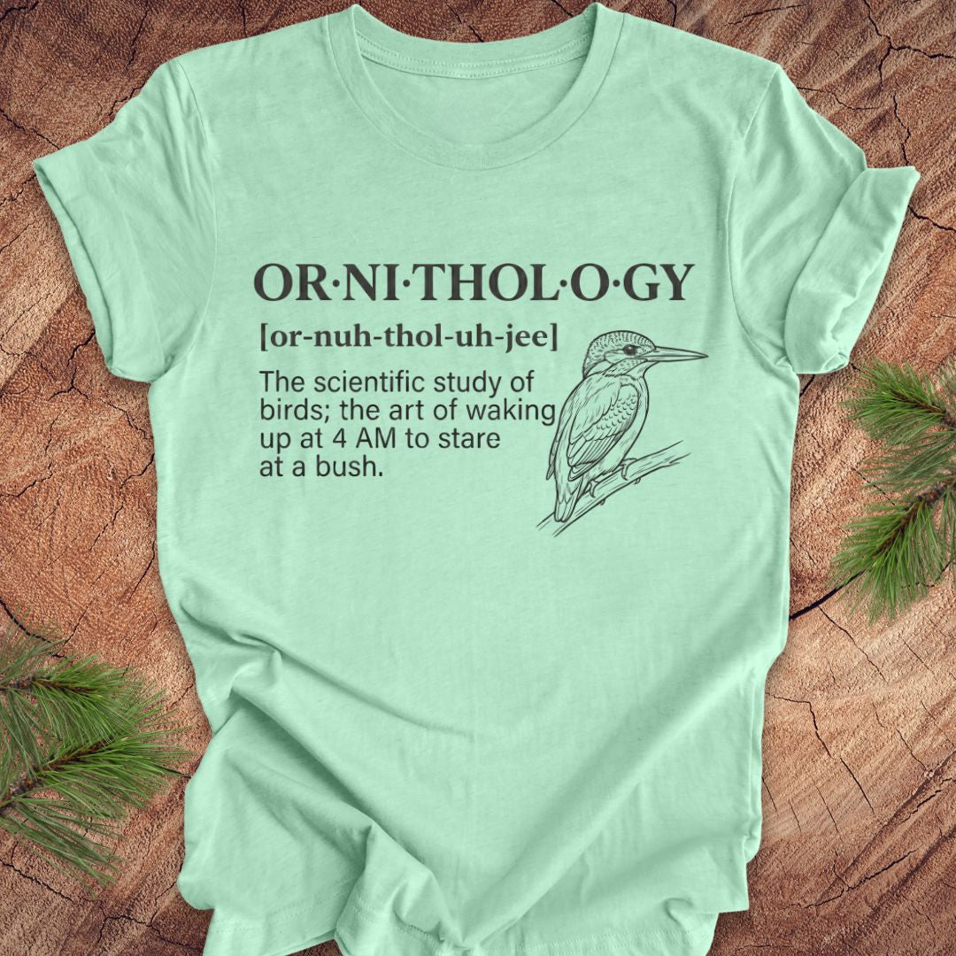 Mint green t-shirt with a funny version of the definition of the word ornithology, with a picture of a bird, on a wood background.