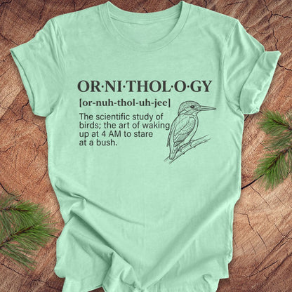 Mint green t-shirt with a funny version of the definition of the word ornithology, with a picture of a bird, on a wood background.