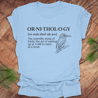 Baby blue t-shirt with a funny version of the definition of the word ornithology, with a picture of a bird, on a wood background.