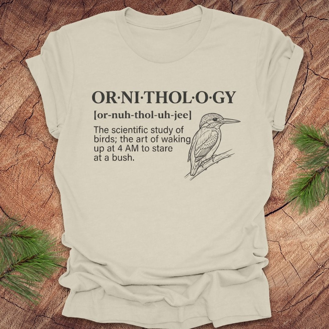 Beige t-shirt with a funny version of the definition of the word ornithology, with a picture of a bird, on a wood background.