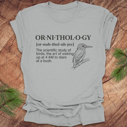Silver t-shirt with a funny version of the definition of the word ornithology, with a picture of a bird, on a wood background.