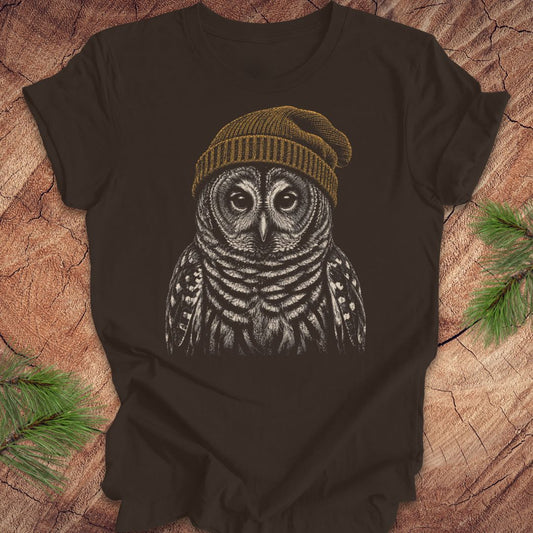 Brown t-shirt with a barred owl wearing a beanie on a wooden surface.