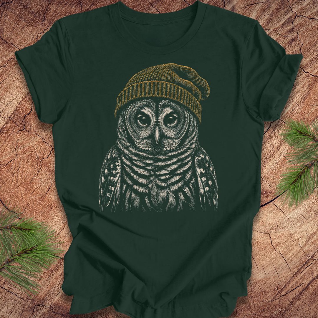 Green t-shirt with a barred owl wearing a beanie on a wooden surface.