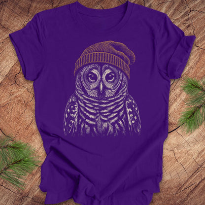 Purple t-shirt with a barred owl wearing a beanie on a wooden surface.