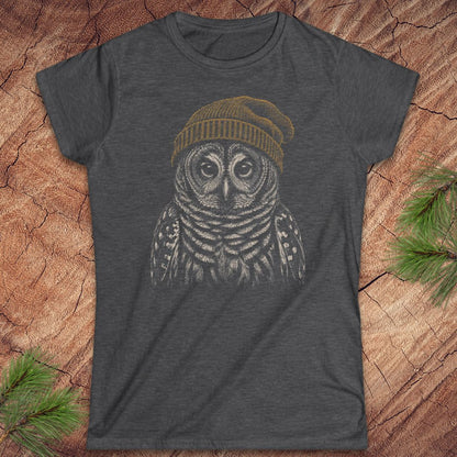 A dark heather gray t-shirt featuring a graphic of an owl wearing a yellow beanie, laid flat on a rustic wood background with pine branches in the corners.