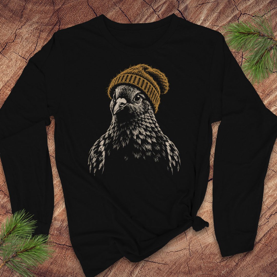 A black long-sleeve t-shirt with a graphic of a bird of prey wearing a mustard yellow knit beanie, laid flat on a rustic wood background with pine branches.