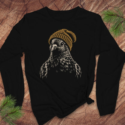 A black long-sleeve t-shirt with a graphic of a bird of prey wearing a mustard yellow knit beanie, laid flat on a rustic wood background with pine branches.
