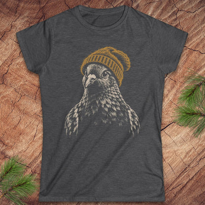 A dark heather gray t-shirt featuring a graphic print of a falcon wearing a yellow knit beanie, laid flat on a rustic wood background with pine needles in the corners.