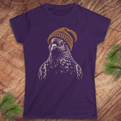 A purple short-sleeve crewneck t-shirt featuring a graphic of a bird of prey wearing a yellow knit beanie, laid flat on a textured wood background with pine branches in the corners.