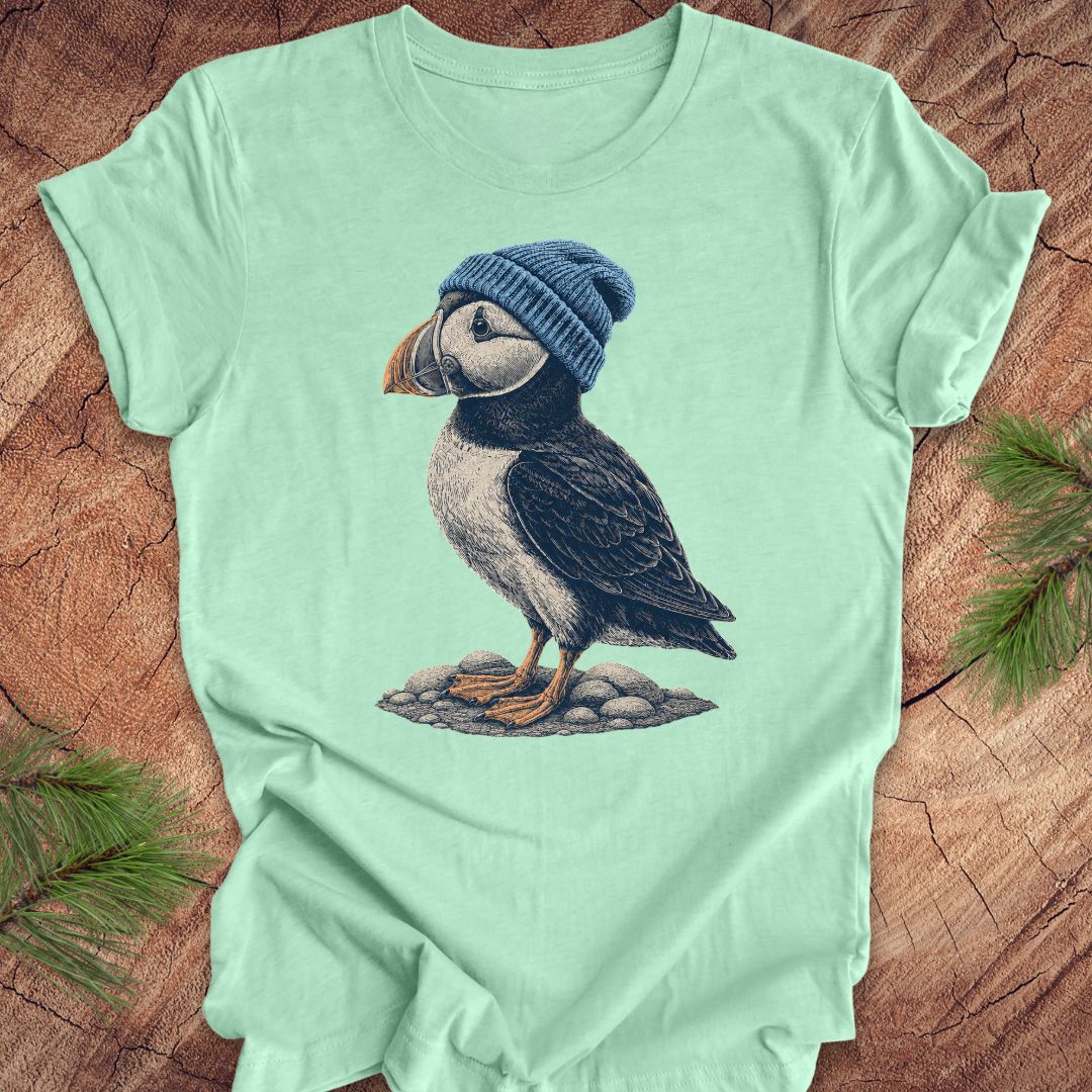 Mint green t-shirt with a puffin wearing a blue beanie on a wooden surface.