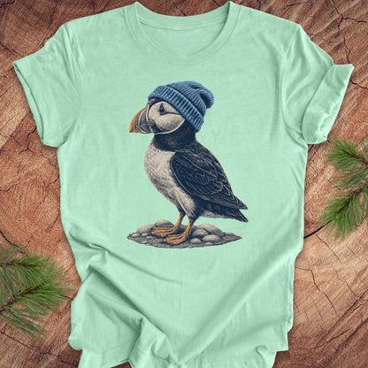 Mint green t-shirt with a puffin wearing a blue beanie on a wooden surface.