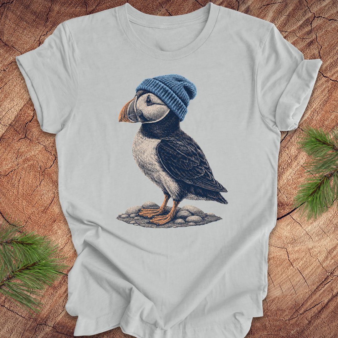 Gray t-shirt with a puffin wearing a blue beanie on a wooden surface.