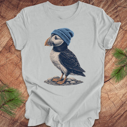 Gray t-shirt with a puffin wearing a blue beanie on a wooden surface.
