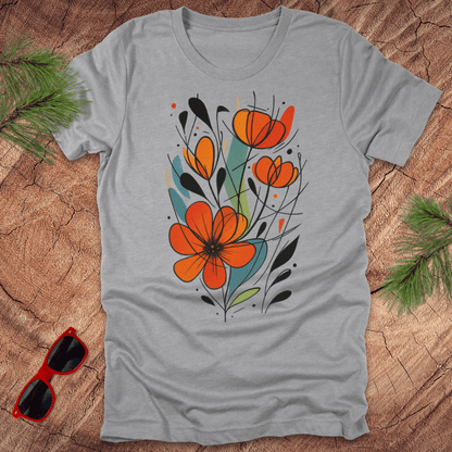 Gray t-shirt with orange floral design on a wooden surface with sunglasses and greenery.