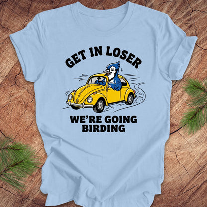 Light blue t-shirt with a graphic of a blue jay driving a yellow car and text on a wooden surface.