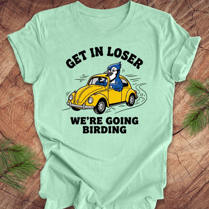 Light green t-shirt with a graphic of a blue jay driving a yellow car and text on a wooden surface.