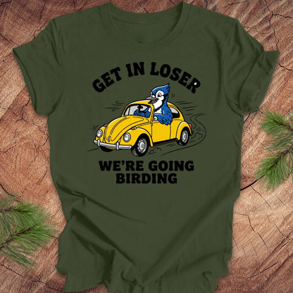 Green t-shirt with a graphic of a blue bird driving a yellow car and text on a wooden surface.