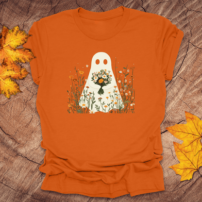 Orange t-shirt with a ghost holding flowers design on a wooden surface with leaves.