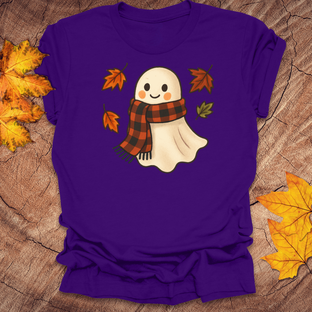 Purple t-shirt with a ghost wearing a plaid scarf design on a wooden surface with autumn leaves.