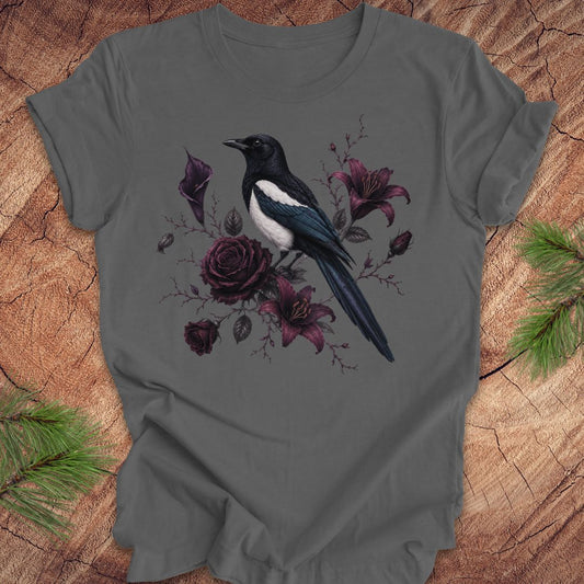 Gray t-shirt with a detailed magpie and purple flowers on a wood background. 