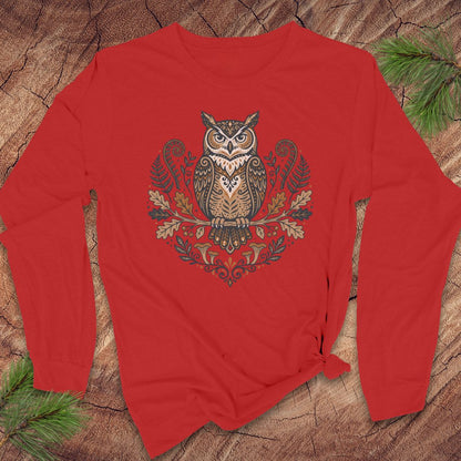 A red long-sleeve t-shirt with a detailed owl graphic on the front, styled flat on a rustic wood background with pine needles.