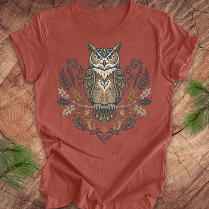 Clay colored t-shirt with an owl and woodland design on a wooden surface