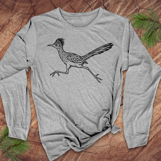 A heather gray long-sleeve t-shirt with a black line art graphic of a roadrunner bird, laid flat on a rustic wood background with pine needles.