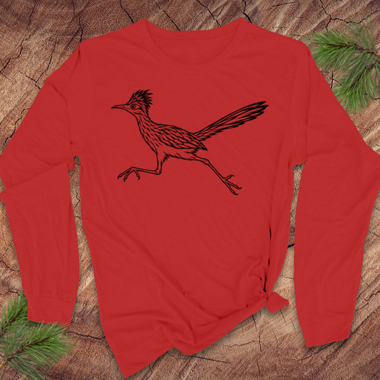 A red long-sleeve t-shirt with a black line art illustration of a roadrunner bird on the chest, styled flat on a rustic wood background with pine needles.