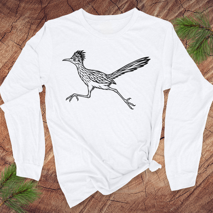 A white long-sleeve t-shirt with a black line art graphic of a running roadrunner, styled flat on a rustic wood background with pine needles.