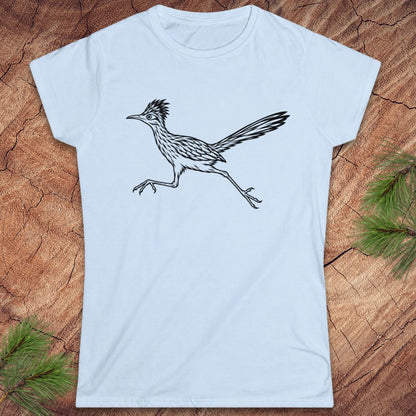 A light blue short-sleeve crewneck t-shirt featuring a black line art illustration of a running roadrunner bird, displayed flat on a rustic wood background with pine needles in the corners.