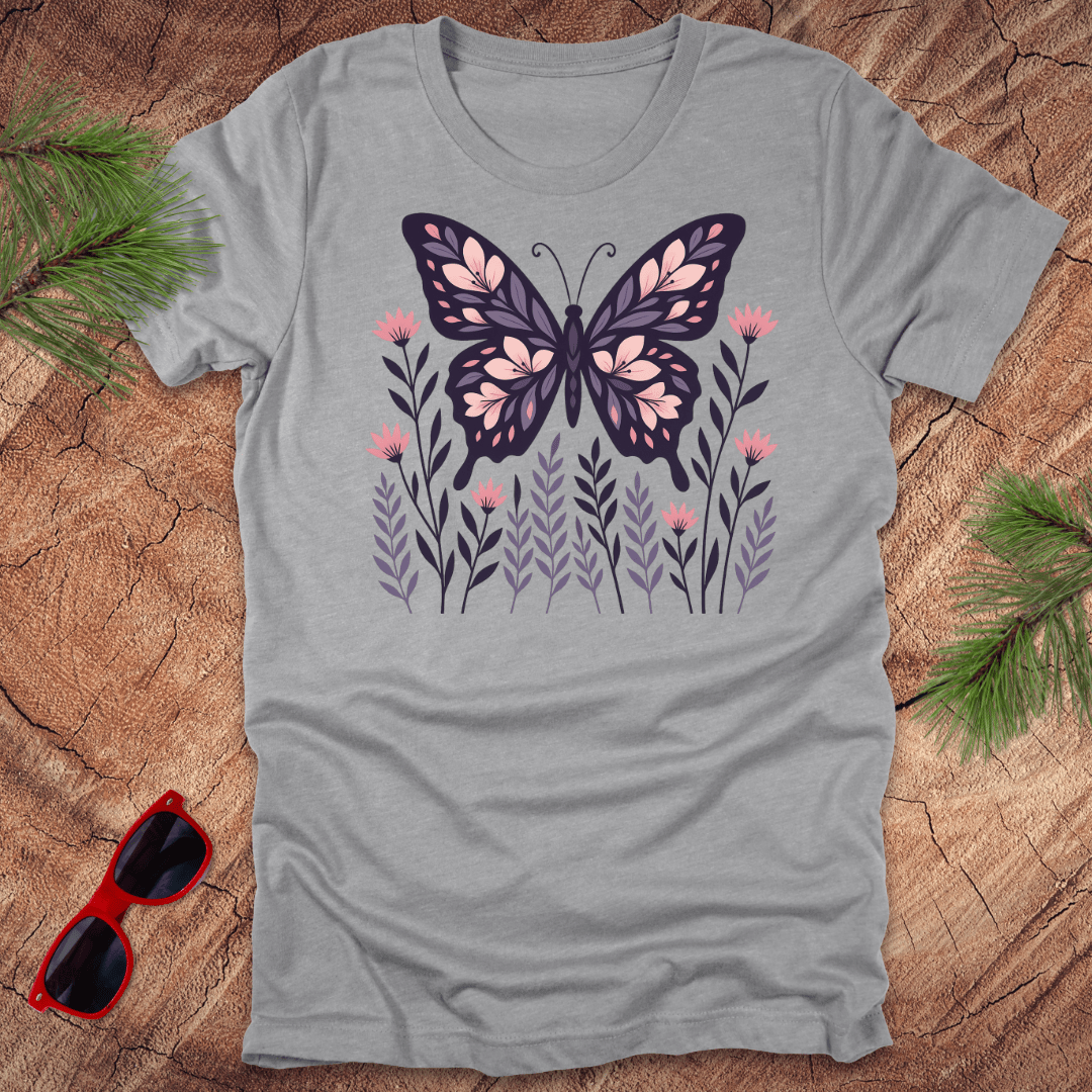 grey t-shirt with a butterfly and flower design on a wooden surface with sunglasses and leaves.