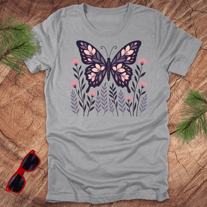 grey t-shirt with a butterfly and flower design on a wooden surface with sunglasses and leaves.