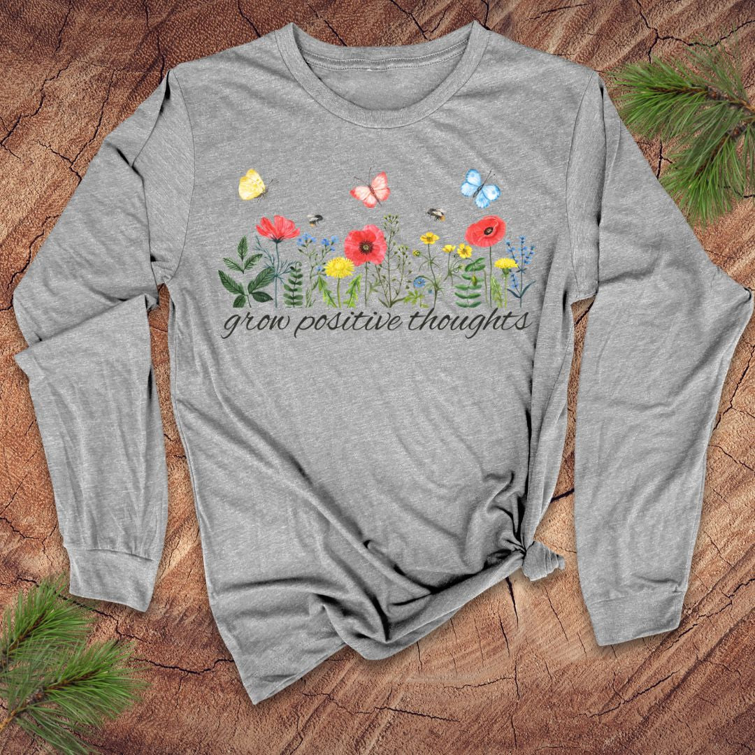 Gray long-sleeve shirt with floral design and "grow positive thoughts' text on a wooden surface