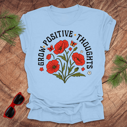 baby blue t-shirt with red flowers and text on a wooden surface with sunglasses and greenery.