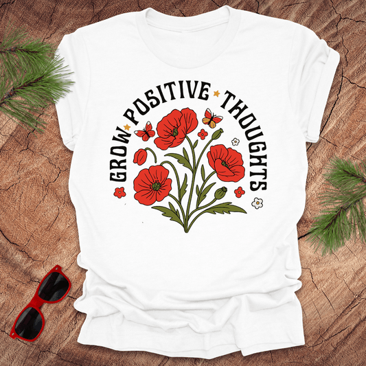 White t-shirt with red floral design and text on a wooden surface with sunglasses and greenery.