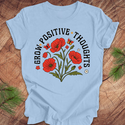 Baby blue t-shirt with red floral design and text 'grow positive thoughts' on a wooden surface 