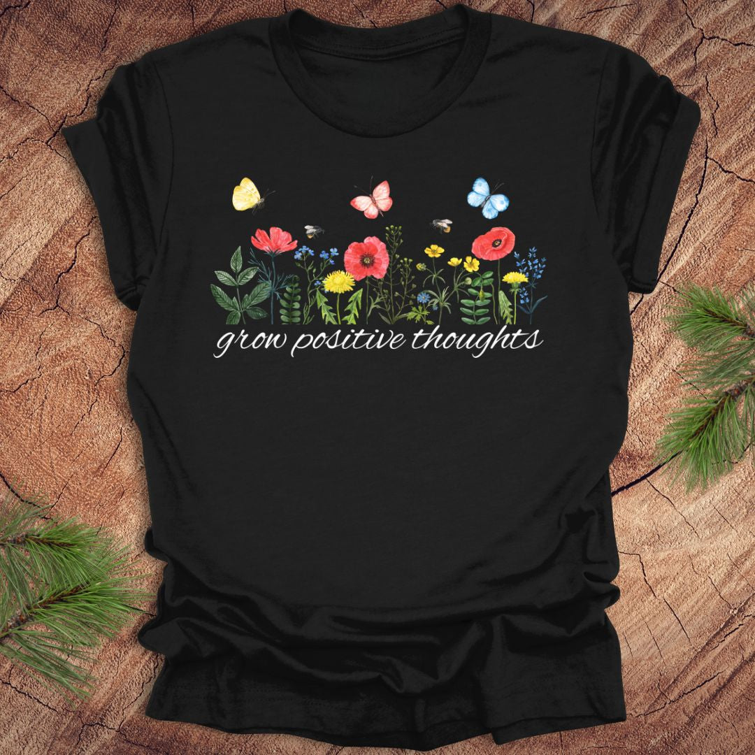 Black t-shirt with floral design and 'grow positive thoughts' text on a wooden surface.