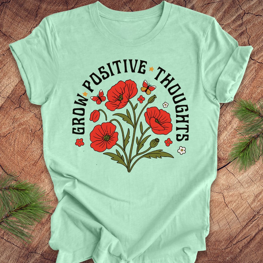Mint green t-shirt with red floral design and text 'grow positive thoughts' on a wooden surface 