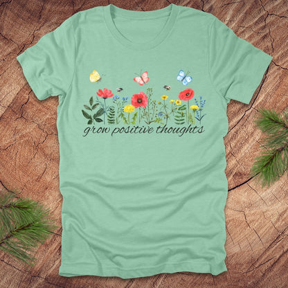 Green t-shirt with floral design and text 'grow positive thoughts' on a wooden surface.