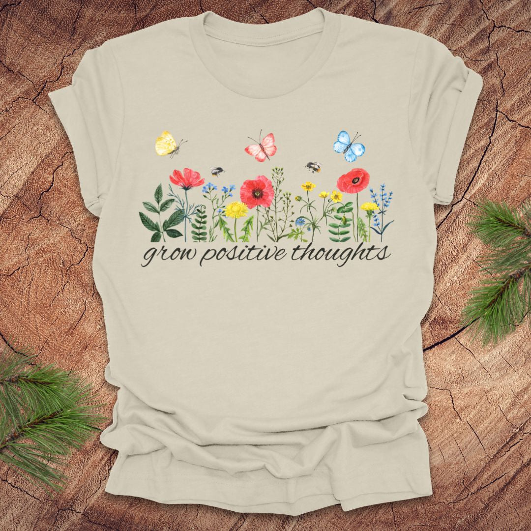 Beige t-shirt with floral design and 'grow positive thoughts' text on a wooden surface.