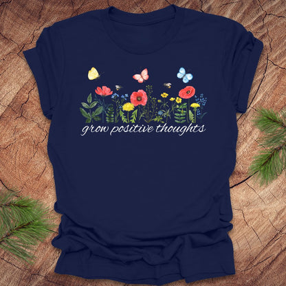 Navy blue t-shirt with floral design and 'grow positive thoughts' text on a wooden surface.