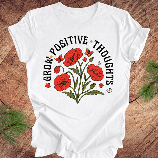 White t-shirt with red floral design and text 'grow positive thoughts' on a wooden surface 