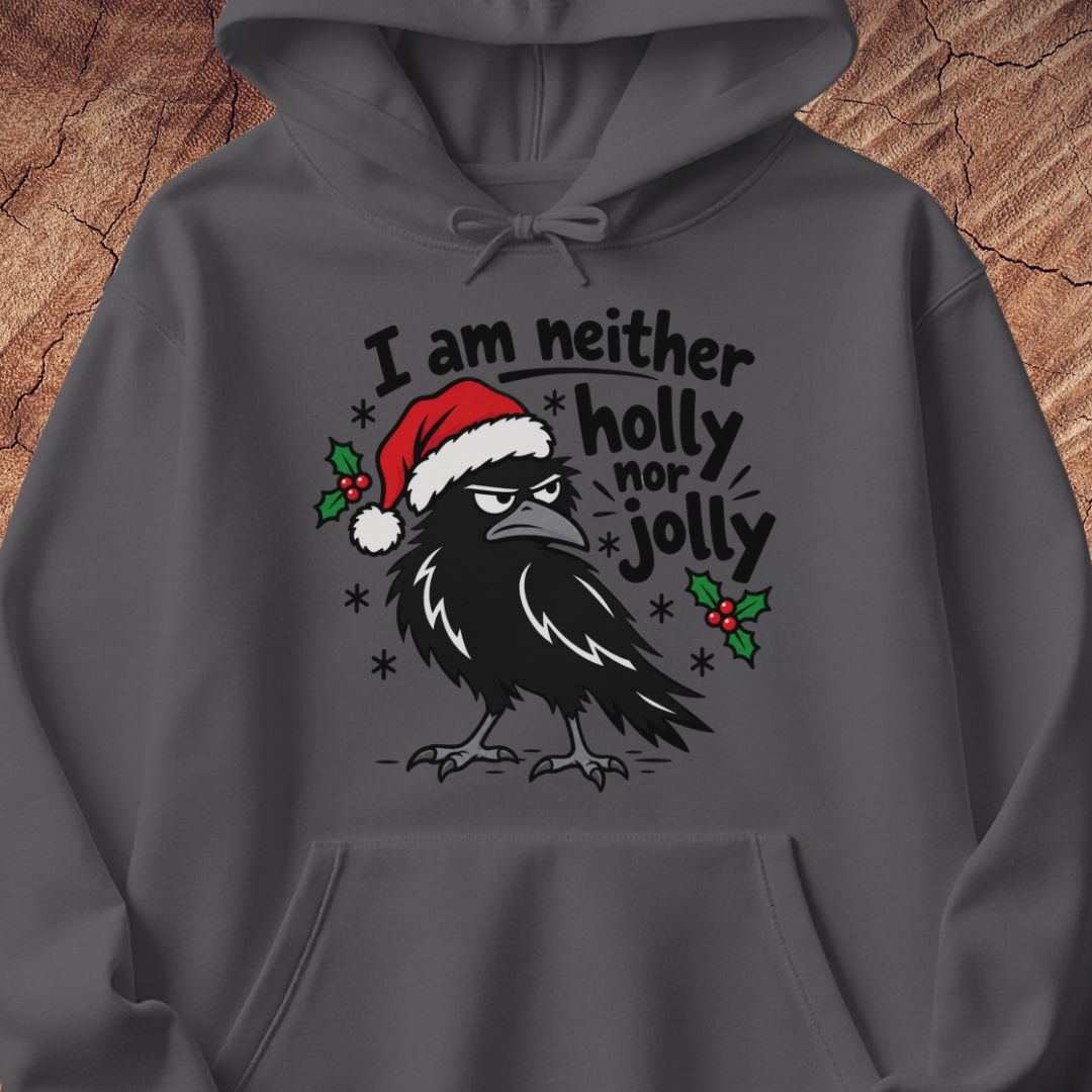 Charcoal gray hoodie with a grumpy raven in a Santa hat surrounded by holly and snowflakes and the words I am neither holly nor jolly, laid flat on a rustic wood background.