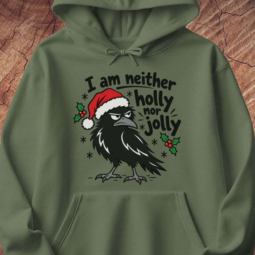 Military green hoodie with a grumpy raven in a Santa hat surrounded by holly and snowflakes and the words I am neither holly nor jolly, laid flat on a rustic wood background.