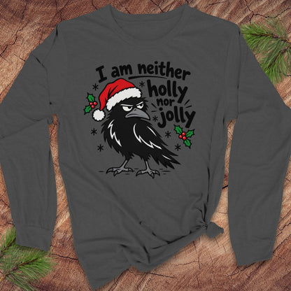Asphalt gray long-sleeve t-shirt with a grumpy raven in a Santa hat surrounded by holly and snowflakes and the words I am neither holly nor jolly, laid flat on a rustic wood background with pine branches.
