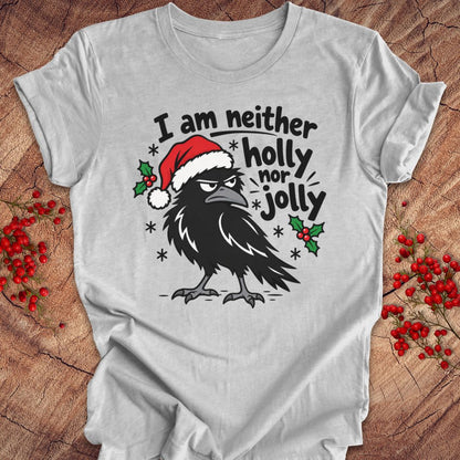 Athletic heather gray t-shirt with a grumpy raven in a Santa hat surrounded by holly and snowflakes and the words I am neither holly nor jolly, laid flat on a rustic wood background with red winter berries.
