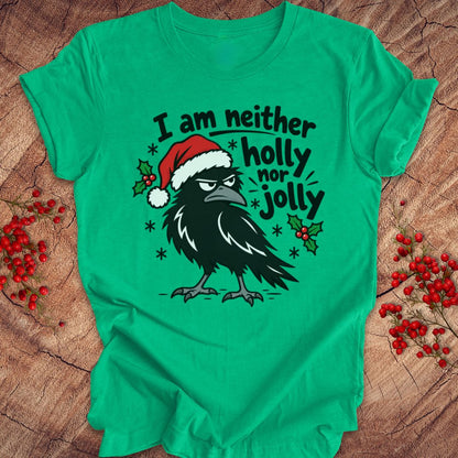 Heather kelly green t-shirt with a grumpy raven in a Santa hat surrounded by holly and snowflakes and the words I am neither holly nor jolly, laid flat on a rustic wood background with red winter berries.