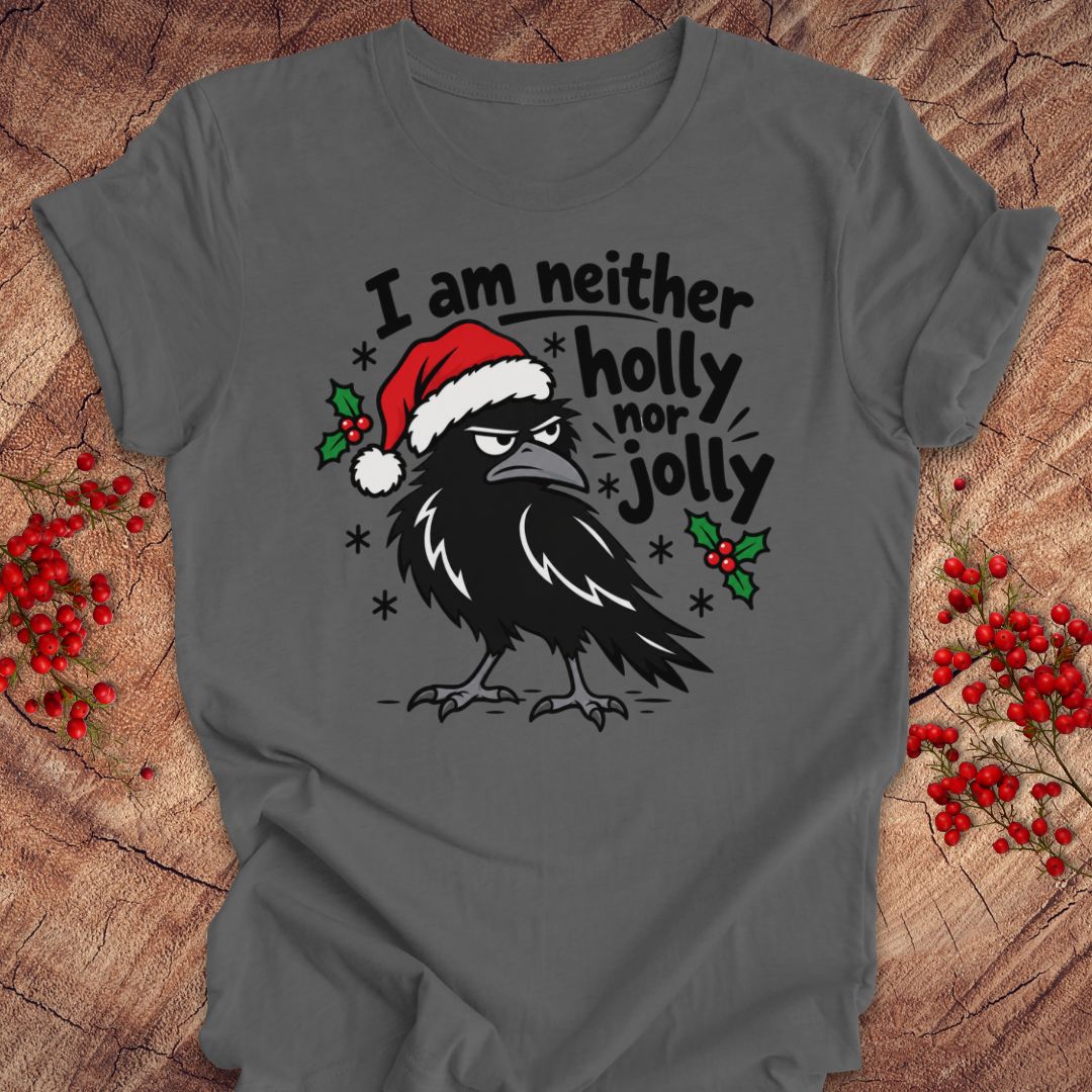 Asphalt gray t-shirt with a grumpy raven in a Santa hat surrounded by holly and snowflakes and the words I am neither holly nor jolly, laid flat on a rustic wood background with red winter berries.